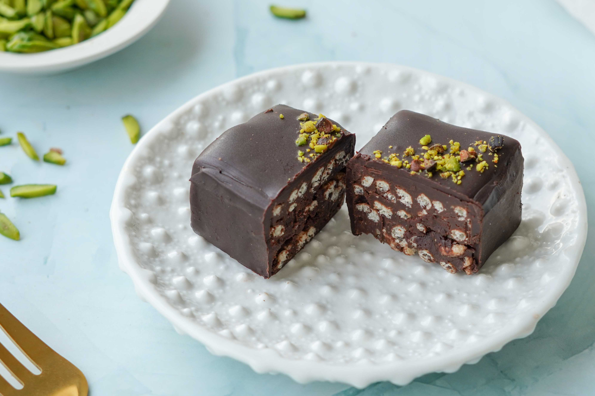 Chocolate dessert with pistachios on a white plate with a light blue background