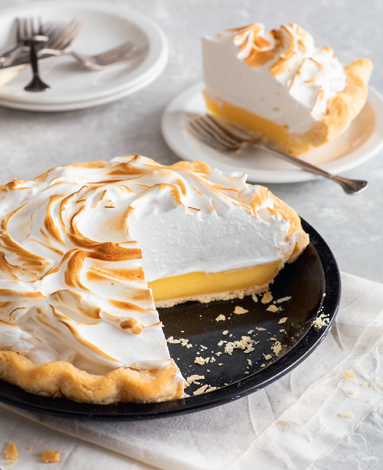 Lemon meringue pie with a slice removed, served on a plate with a fork.