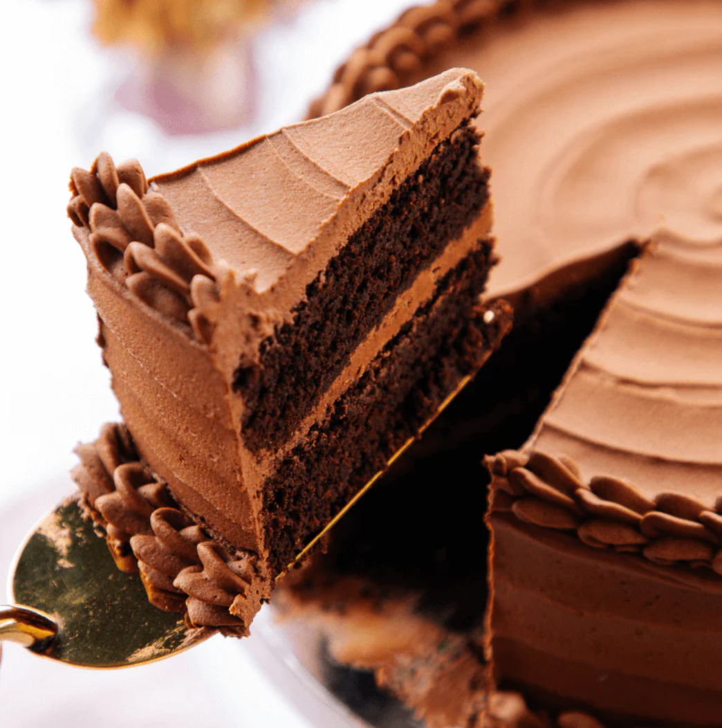Chocolate cake with a slice cut out, showing layers and frosting on a white background.