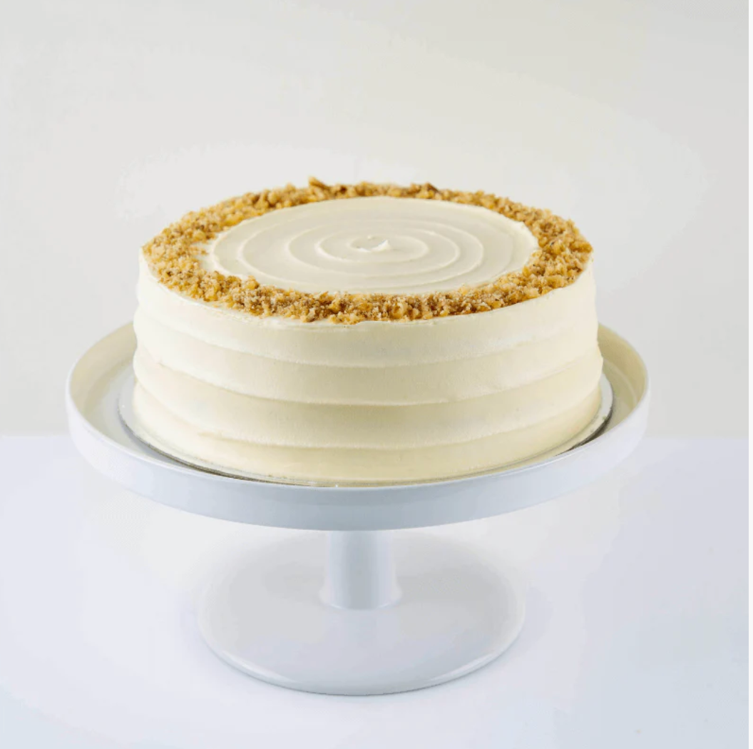 Cake with white frosting and crumbly topping on a white cake stand against a white background