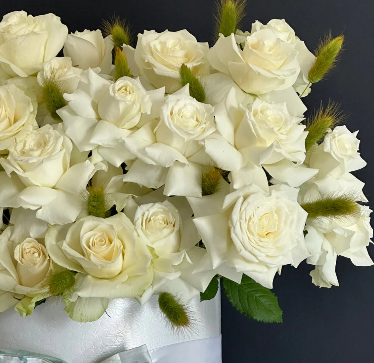 Bouquet of white roses with green leaves on a dark background