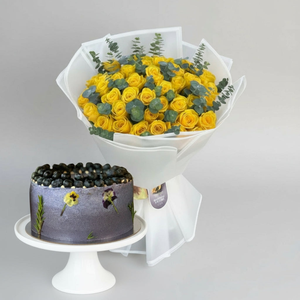Bouquet of yellow roses with greenery and a cake on a light gray background