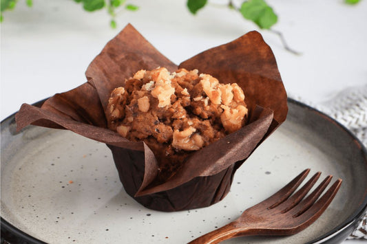 Muffin in a brown paper liner on a speckled plate with a wooden fork.
