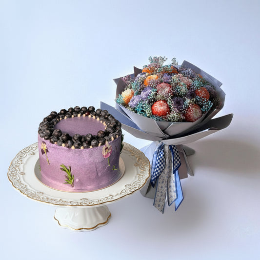 Purple cake with berry decoration and a bouquet of frosted berries on a light blue background