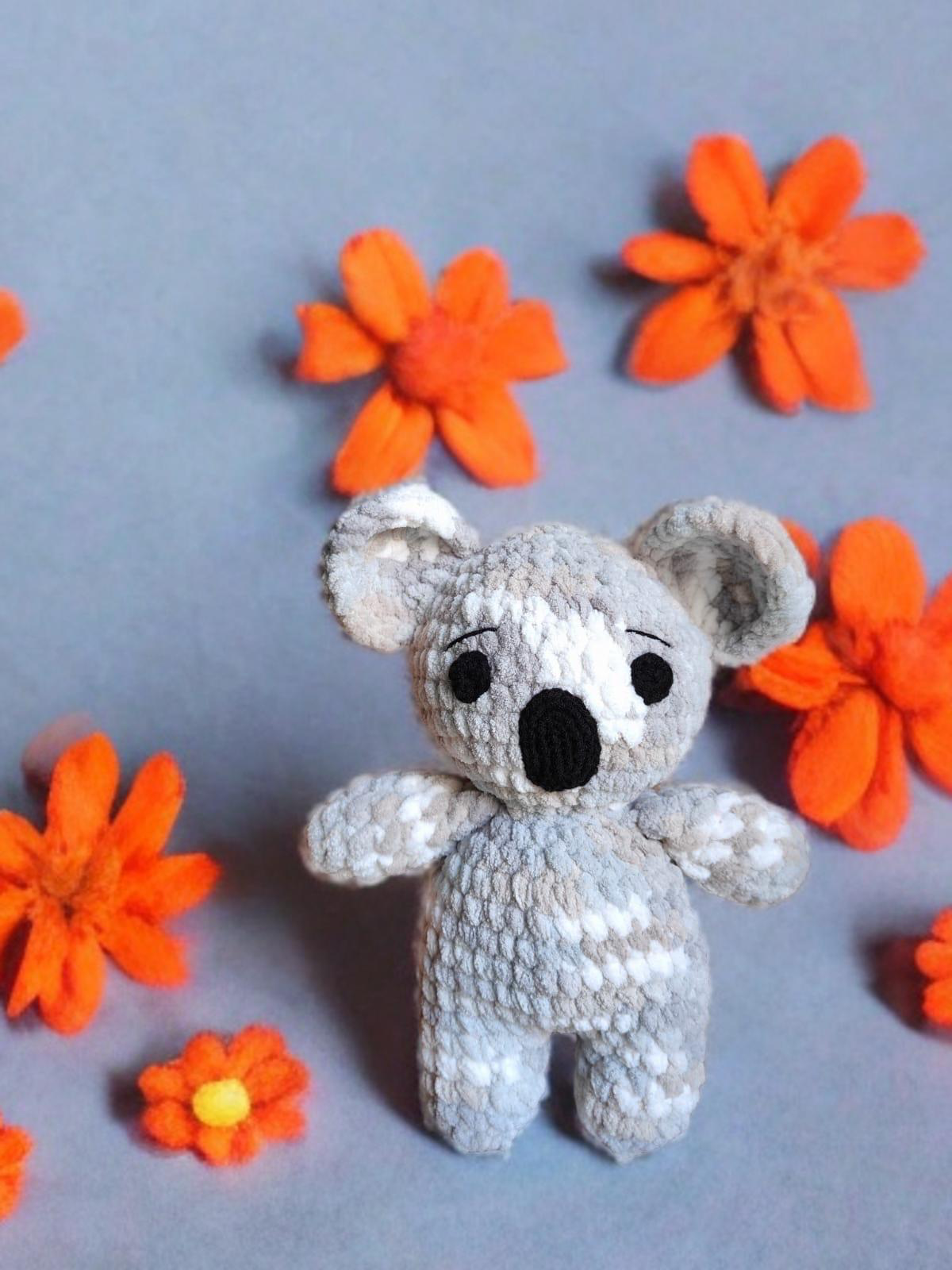 Crocheted koala toy with orange flowers on a gray background
