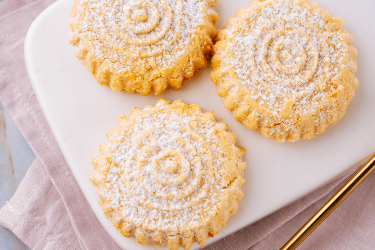 Three cookies with a spiral pattern on a white plate, dusted with powdered sugar.