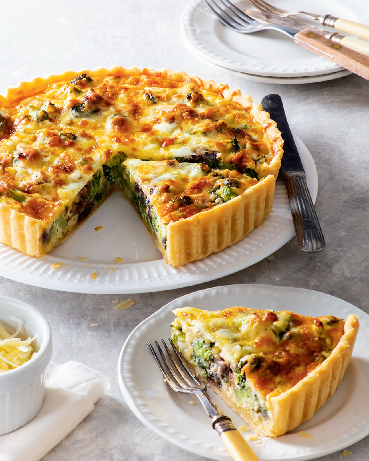Quiche with a slice removed, served on a plate with a fork, on a light gray surface.