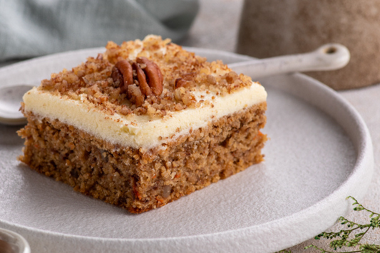 Square slice of carrot cake with cream cheese frosting on a white plate.