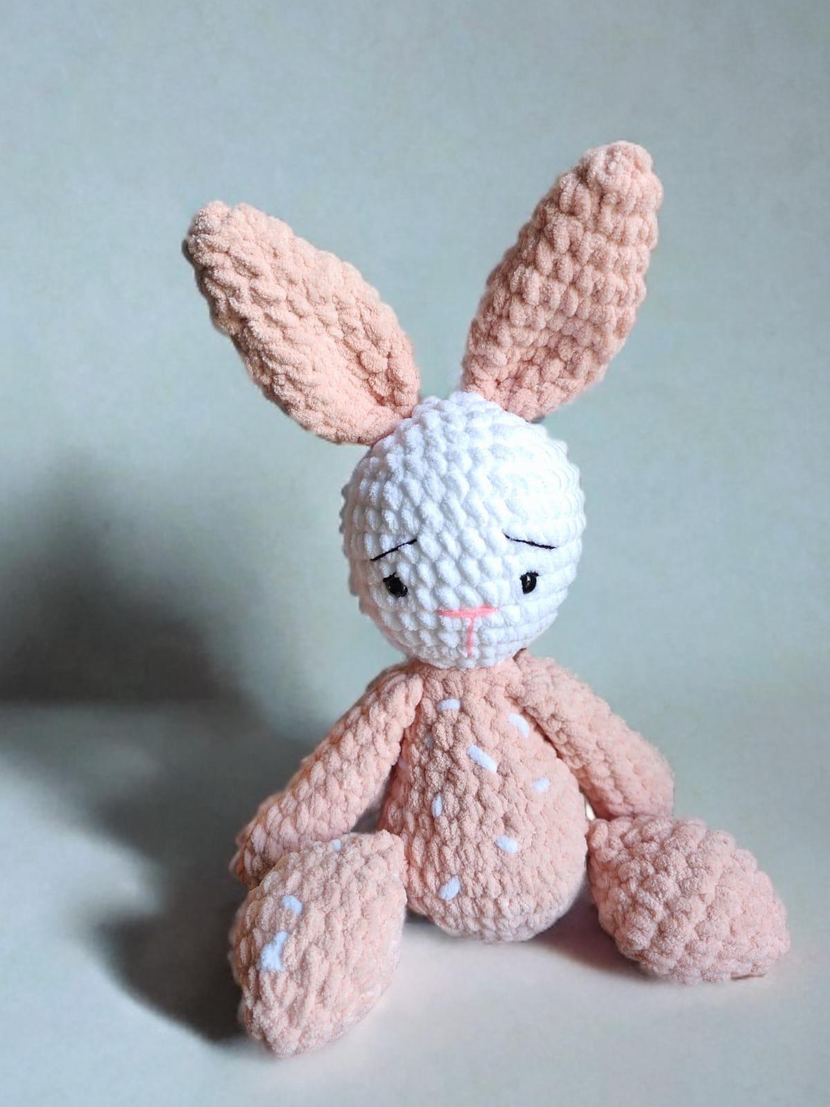 Pink crochet bunny toy with a white face on a light blue background