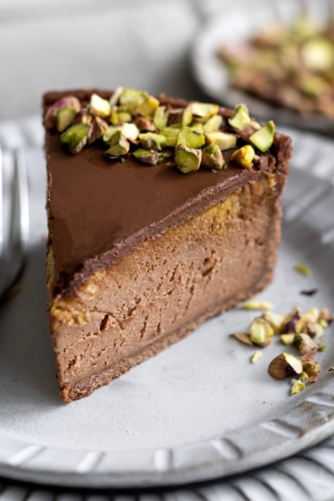 Slice of gluten-free vegan chocolate cheesecake with pistachio nuts on a white plate