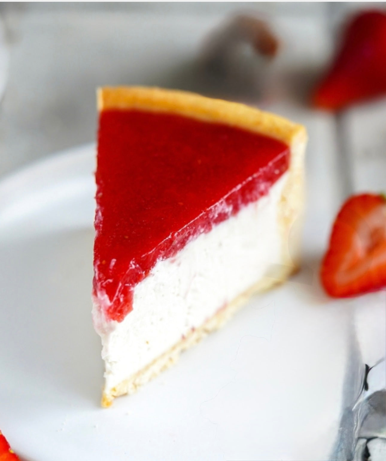 Slice of gluten-free vegan strawberry cheesecake on a white plate with strawberries around