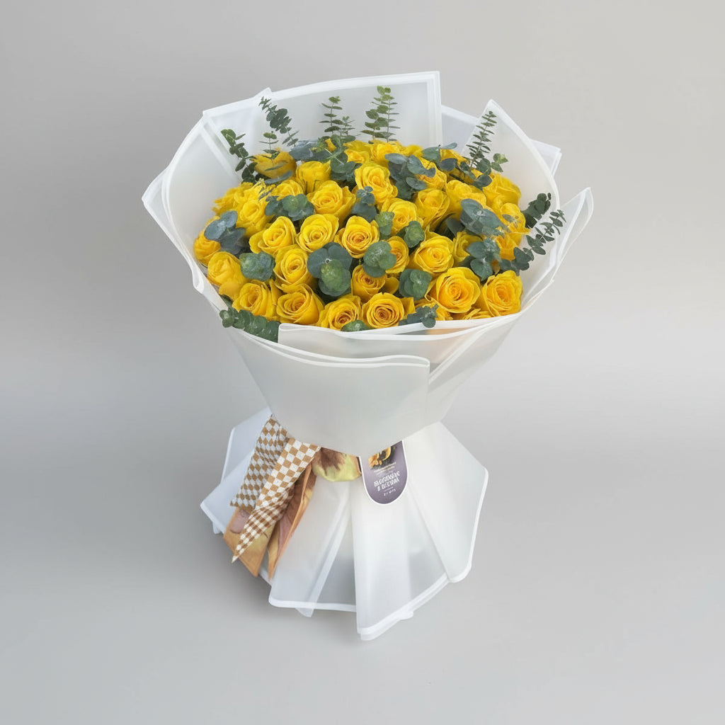 Bouquet of yellow roses with greenery in a white wrap on a light gray surface