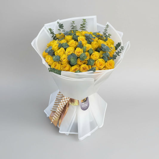 Bouquet of yellow roses with greenery in a white wrap on a light gray surface