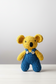 Crocheted toy bear with yellow body and blue overalls on a plain background