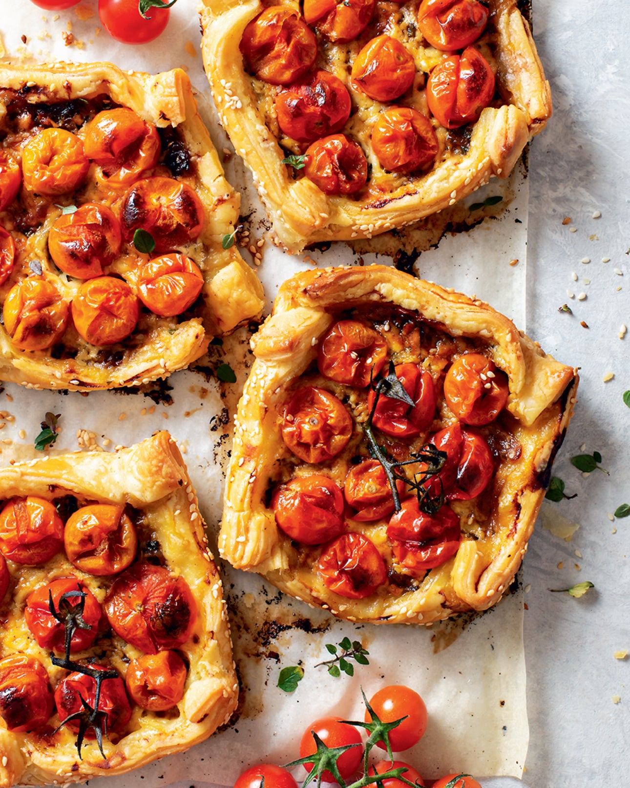Tomato tarts on a baking tray with fresh tomatoes around