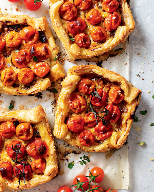 Tomato tarts on a baking tray with fresh tomatoes around