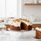 Carrot cake with cream cheese frosting on a stand in a kitchen setting
