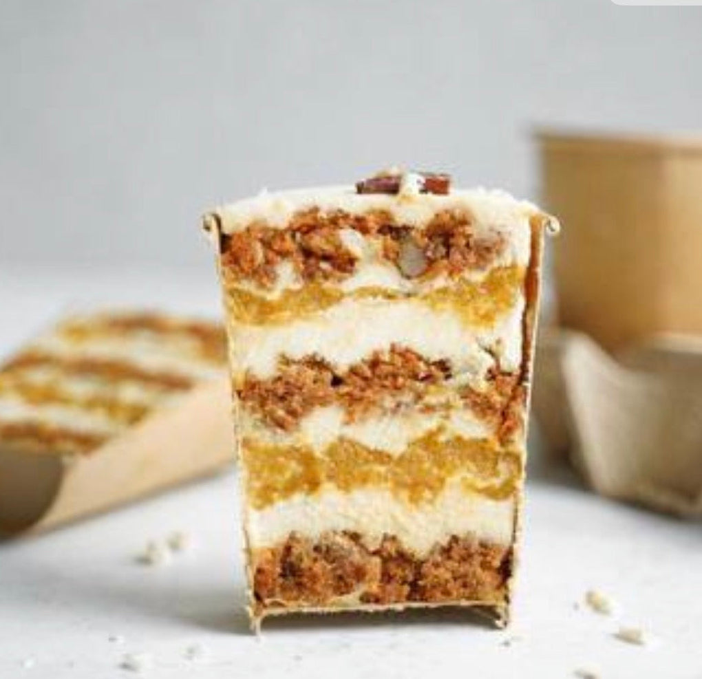Layered dessert bar with a white creamcheese filling and carrot cake crumbly top, on a light gray background.