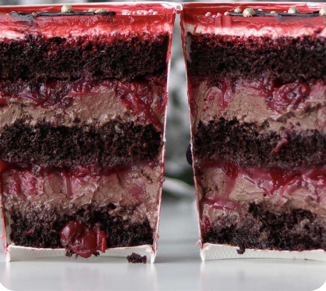 Two slices of layered chocolate cake with cherry filling on a white marble surface.