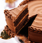 Chocolate cake with a slice cut out, showing layers and frosting on a white background.