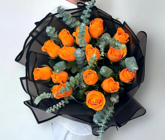 Bouquet of orange roses with greenery in a black wrap on a white background