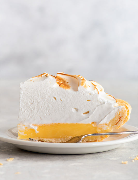 Slice of lemon meringue pie on a plate with a gray background
