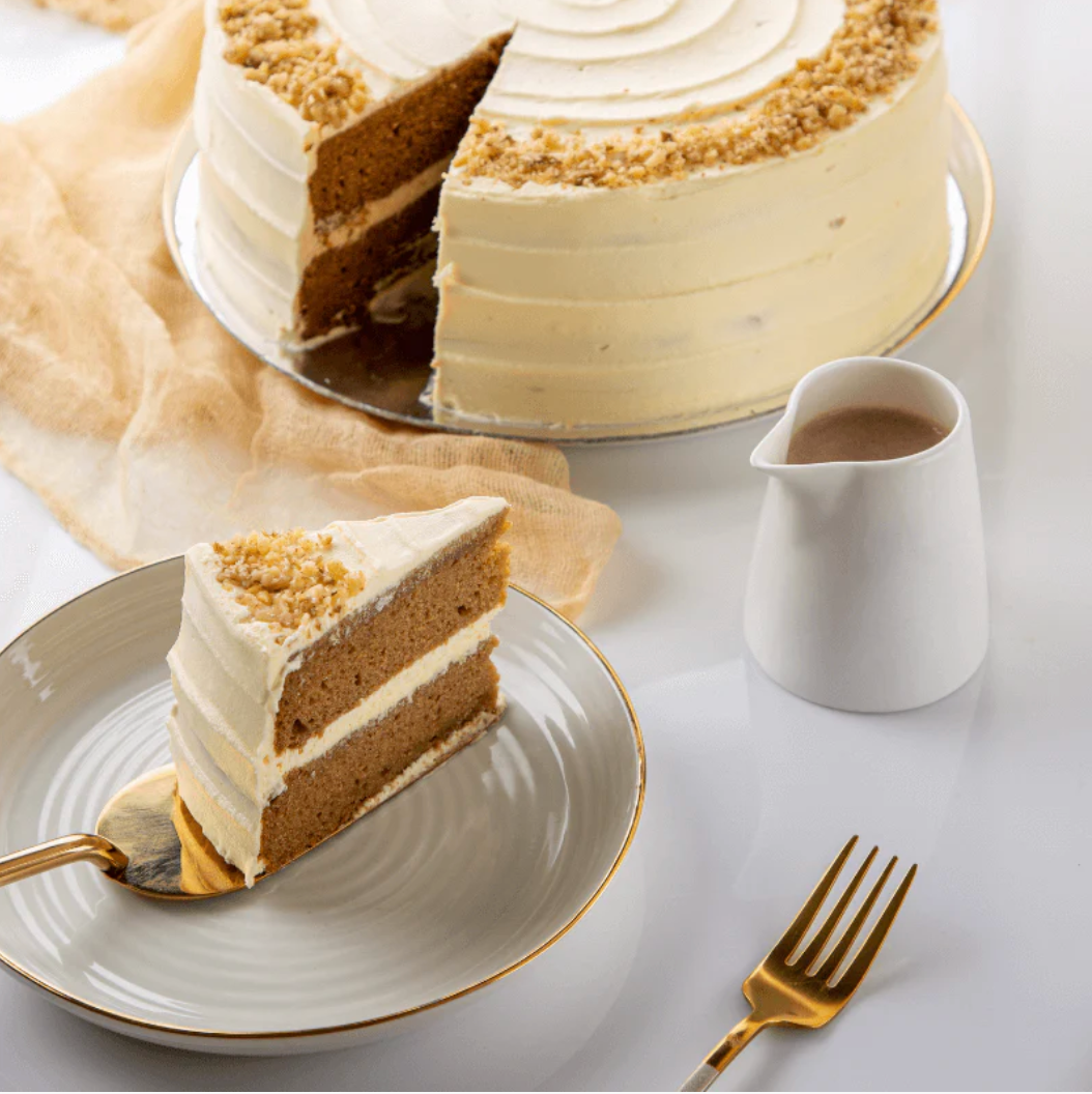 Layered cake with a slice on a plate, accompanied by a small pitcher and fork on a light background