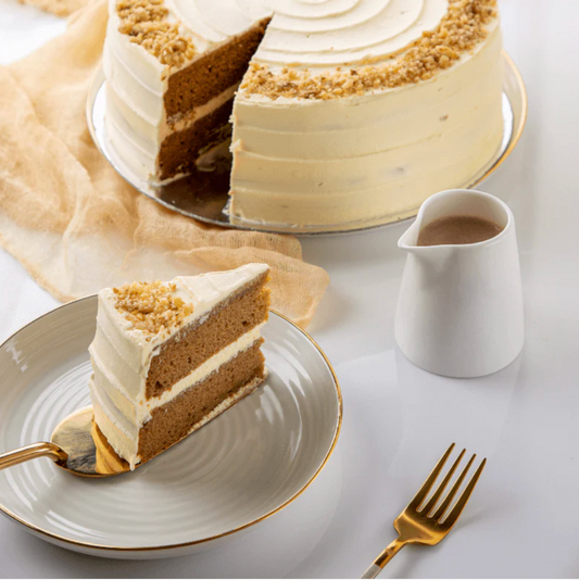 Layered cake with a slice on a plate, accompanied by a small pitcher and fork on a light background