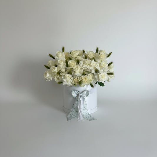 Bouquet of white roses in a white box with a decorative bow on a light gray background