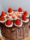A chocolate cake with multiple layers, decorated with strawberries on top and covered with white frosting.