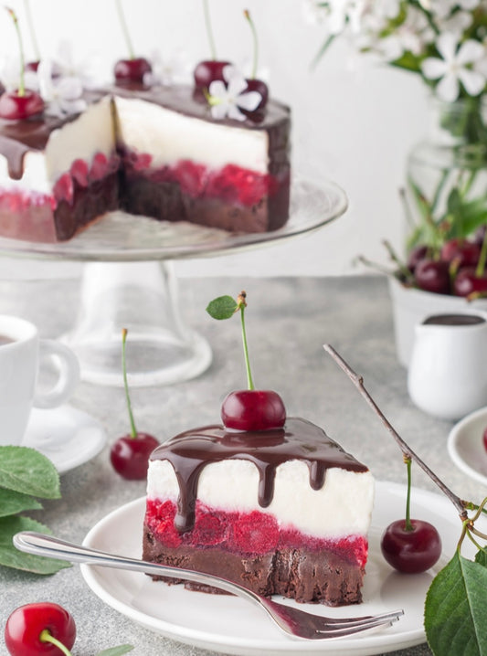 A slice of black forest ice cream cake with cherries and dark chocolate on top, served on a plate with a fork, against a background of flowers and leaves.